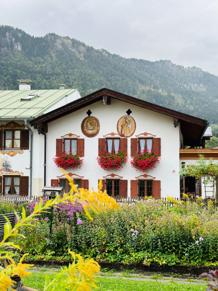 Picturesque Bavarian house adorned with vibrant flowers and unique wall art, set amidst lush greenery.