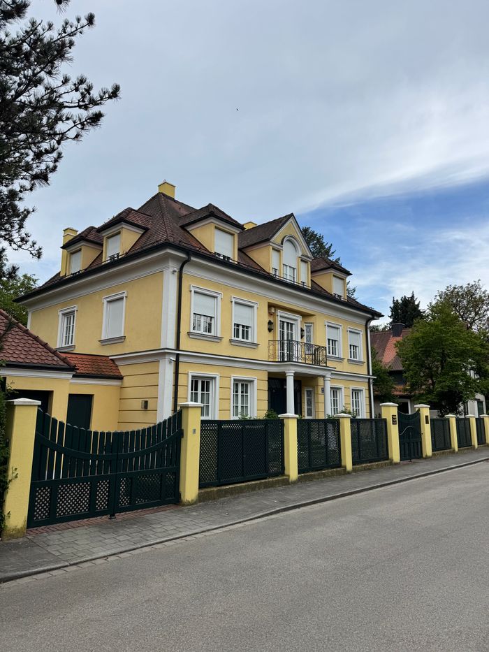 A beautiful yellow villa with a classic design located in a suburban area of Munich, Germany.
